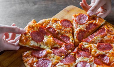 iki kadın elini tutuyor bir dilim biberli Pizza Mozzarella peynir, salam, domates, biber. Ahşap masa arka plan üzerinde İtalyan pizza