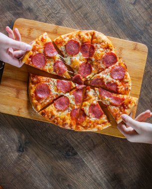 iki kadın elini tutuyor bir dilim biberli Pizza Mozzarella peynir, salam, domates, biber. Ahşap masa arka plan üzerinde İtalyan pizza