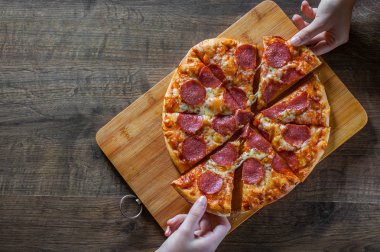 iki kadın elini tutuyor bir dilim biberli Pizza Mozzarella peynir, salam, domates, biber. Ahşap masa arka plan üzerinde İtalyan pizza