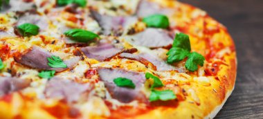 Pizza Mozzarella peyniri, jambon, biber, et, domates sosu, baharat ve taze fesleğen. Ahşap arka plan üzerinde İtalyan pizza