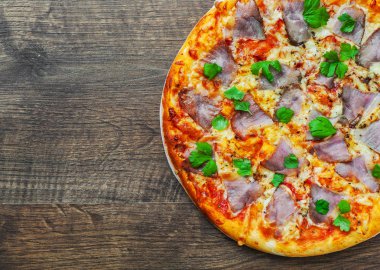 Pizza Mozzarella peyniri, jambon, biber, et, domates sosu, baharat ve taze fesleğen. Ahşap arka plan üzerinde İtalyan pizza