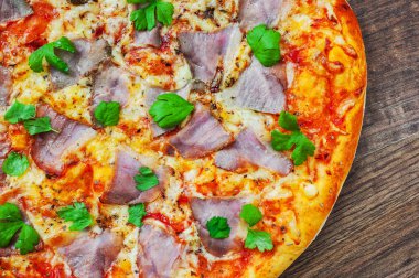 Pizza Mozzarella peyniri, jambon, biber, et, domates sosu, baharat ve taze fesleğen. Ahşap arka plan üzerinde İtalyan pizza