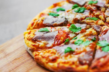 Pizza Mozzarella peyniri, jambon, biber, et, domates sosu, baharat ve taze fesleğen. Ahşap arka plan üzerinde İtalyan pizza