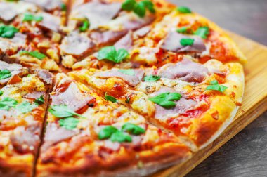 Pizza Mozzarella peyniri, jambon, biber, et, domates sosu, baharat ve taze fesleğen. Ahşap arka plan üzerinde İtalyan pizza