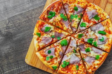 Pizza Mozzarella peyniri, jambon, biber, et, domates sosu, baharat ve taze fesleğen. Ahşap arka plan üzerinde İtalyan pizza