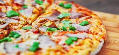 Pizza Mozzarella peyniri, jambon, biber, et, domates sosu, baharat ve taze fesleğen. Ahşap arka plan üzerinde İtalyan pizza