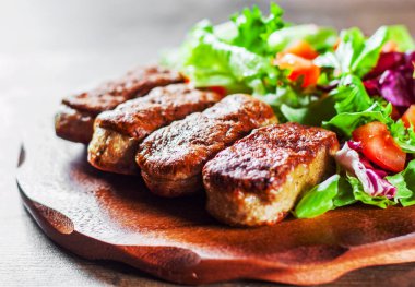 Kızarmış sosis ve domates plaka ile ahşap masa arka plan üzerinde çeşitli taze karışımı salata yaprakları