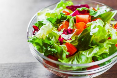 ahşap arka plan üzerinde cam kapta domates ile çeşitli taze karışımı salata yaprakları.