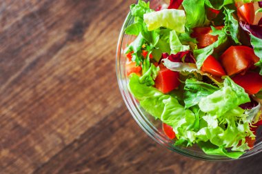 ahşap arka plan üzerinde cam kapta domates ile çeşitli taze karışımı salata yaprakları.