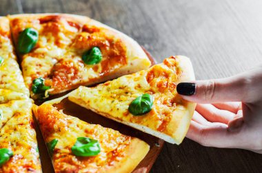 Kadın el alır bir dilim Pizza Mozzarella peynir, domates, biber, baharat ve taze fesleğen. İtalyan pizza. Pizza Margherita veya ahşap masa arka plan üzerinde Margarita