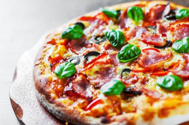 Pizza Mozzarella peyniri, jambon, biber, zeytin, et, domates sosu, baharat ve taze fesleğen. Ahşap arka plan üzerinde İtalyan pizza