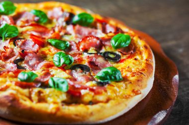 Pizza Mozzarella peyniri, jambon, biber, zeytin, et, domates sosu, baharat ve taze fesleğen. Ahşap arka plan üzerinde İtalyan pizza
