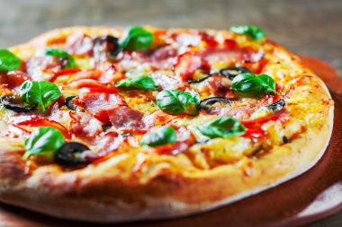 Pizza Mozzarella peyniri, jambon, biber, zeytin, et, domates sosu, baharat ve taze fesleğen. Ahşap arka plan üzerinde İtalyan pizza