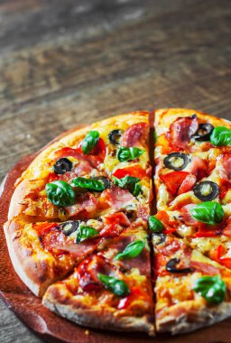 Pizza Mozzarella peyniri, jambon, biber, zeytin, et, domates sosu, baharat ve taze fesleğen. Ahşap arka plan üzerinde İtalyan pizza