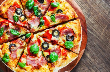 Pizza Mozzarella peyniri, jambon, biber, zeytin, et, domates sosu, baharat ve taze fesleğen. Ahşap arka plan üzerinde İtalyan pizza