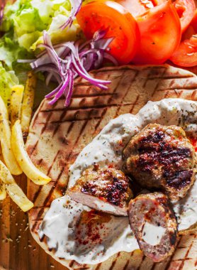 Spicy bifteki, frikadelle or frikkadel meatballs with minced beef and lamb with pita bread, tzatziki dip, vegetables salad and French fries. Greek meatballs keftedes or Keftedakia with feta
