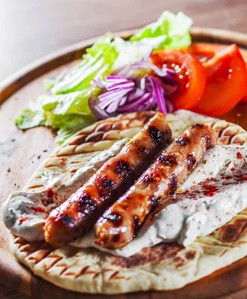 grilled meat sausages with pita bread and vegetables salad and tzatziki dip on wooden board