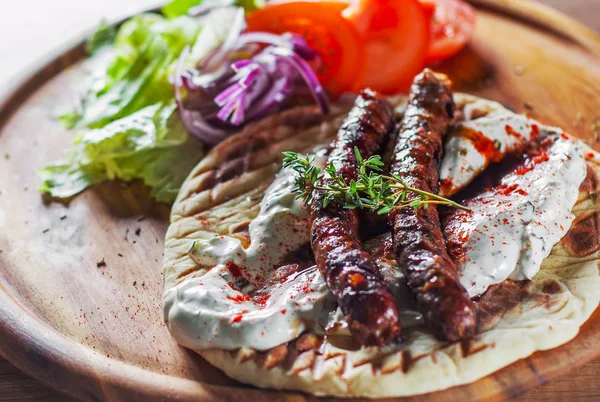 grilled meat sausages with pita bread and vegetables salad and tzatziki dip on wooden board