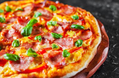 Pizza Mozzarella peyniri, jambon, biber, et, domates sosu, baharat ve taze fesleğen. Siyah arka plan üzerine İtalyan pizza