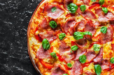 Pizza Mozzarella peyniri, jambon, biber, et, domates sosu, baharat ve taze fesleğen. Siyah arka plan üzerine İtalyan pizza