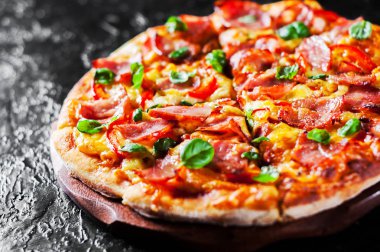 Pizza Mozzarella peyniri, jambon, biber, et, domates sosu, baharat ve taze fesleğen. Siyah arka plan üzerine İtalyan pizza