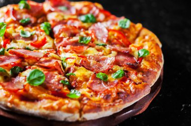 Pizza Mozzarella peyniri, jambon, biber, et, domates sosu, baharat ve taze fesleğen. Siyah arka plan üzerine İtalyan pizza