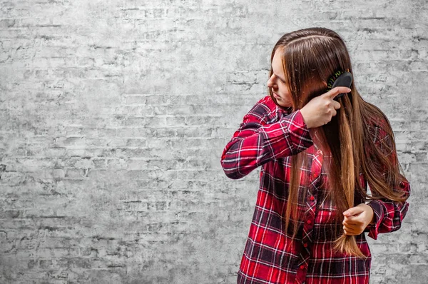 灰色の壁の背景に彼女の髪をとかす髪の長い若いティーネー ジャーのブルネットの少女の肖像画 — ストック写真