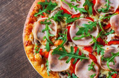 Pizza Mozzarella peyniri, mantar, jambon, domates sosu, biber, baharat ve taze roka. Ahşap masa arka plan üzerinde İtalyan pizza