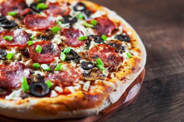 Mozzarella peyniri, salam, biber, biber, zeytin, baharat ve mantar pizza. Ahşap masa arka plan üzerinde İtalyan pizza