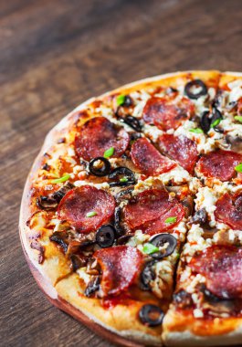 Mozzarella peyniri, salam, biber, biber, zeytin, baharat ve mantar pizza. Ahşap masa arka plan üzerinde İtalyan pizza