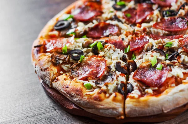 Mozzarella peyniri, salam, biber, biber, zeytin, baharat ve mantar pizza. Ahşap masa arka plan üzerinde İtalyan pizza