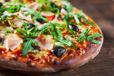 Pizza Mozzarella peyniri, mantar, jambon, domates sosu, biber, zeytin, baharatlar ve taze roka. Ahşap masa arka plan üzerinde İtalyan pizza