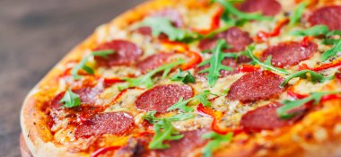 Mozzarella peyniri, salam, domates, biber, baharat ve taze roka ile biberli Pizza. Ahşap masa arka plan üzerinde İtalyan pizza