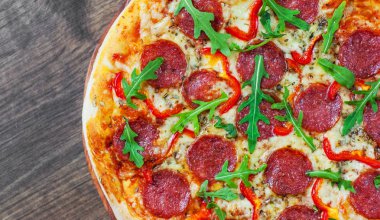 Mozzarella peyniri, salam, domates, biber, baharat ve taze roka ile biberli Pizza. Ahşap masa arka plan üzerinde İtalyan pizza