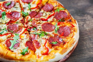 Mozzarella peyniri, salam, domates, biber, baharat ve taze roka ile biberli Pizza. Ahşap masa arka plan üzerinde İtalyan pizza