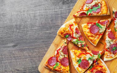 Mozzarella peyniri, salam, domates, biber, baharat ve taze roka ile biberli Pizza. Ahşap masa arka plan üzerinde İtalyan pizza