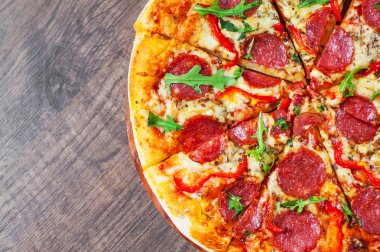 Mozzarella peyniri, salam, domates, biber, baharat ve taze roka ile biberli Pizza. Ahşap masa arka plan üzerinde İtalyan pizza