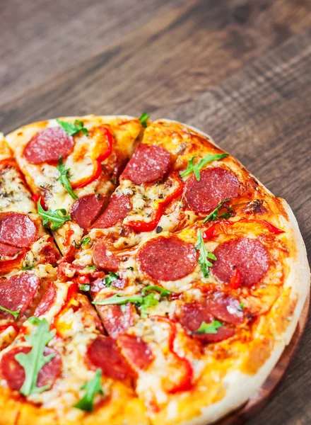 Mozzarella peyniri, salam, domates, biber, baharat ve taze roka ile biberli Pizza. Ahşap masa arka plan üzerinde İtalyan pizza