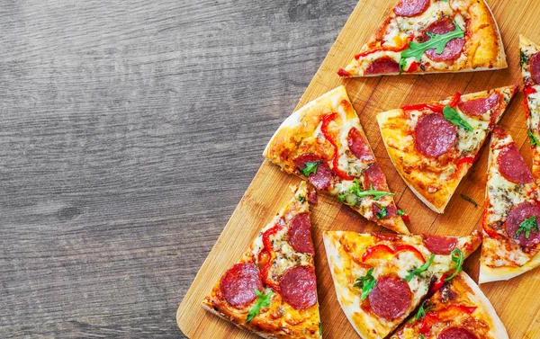 Mozzarella peyniri, salam, domates, biber, baharat ve taze roka ile biberli Pizza. Ahşap masa arka plan üzerinde İtalyan pizza