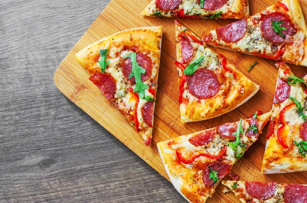 Mozzarella peyniri, salam, domates, biber, baharat ve taze roka ile biberli Pizza. Ahşap masa arka plan üzerinde İtalyan pizza