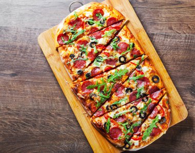 Pizza Mozzarella peyniri, salam, biber, biber, zeytin, baharatlar ve taze roka ile. Ahşap masa arka plan üzerinde İtalyan pizza