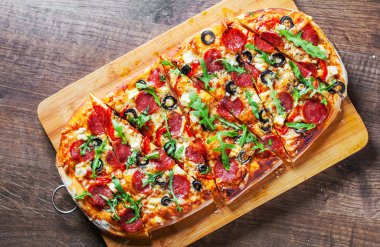 Pizza Mozzarella peyniri, salam, biber, biber, zeytin, baharatlar ve taze roka ile. Ahşap masa arka plan üzerinde İtalyan pizza