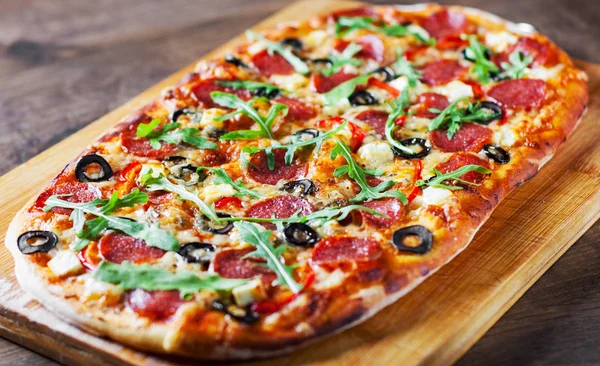 Pizza with Mozzarella cheese, salami, pepper, pepperoni, olives, Spices and Fresh arugula. Italian pizza on wooden table background