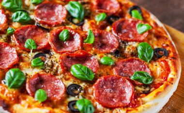Pepperoni Pizza Mozzarella peyniri, salam, domates, zeytin, biber, baharat ve taze fesleğen. Ahşap masa arka plan üzerinde İtalyan pizza