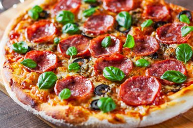Pepperoni Pizza Mozzarella peyniri, salam, domates, zeytin, biber, baharat ve taze fesleğen. Ahşap masa arka plan üzerinde İtalyan pizza