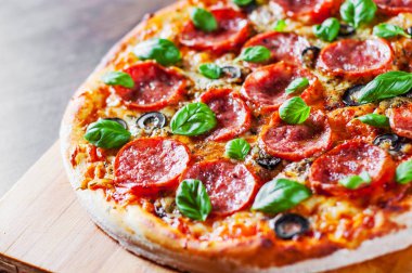 Pepperoni Pizza Mozzarella peyniri, salam, domates, zeytin, biber, baharat ve taze fesleğen. Ahşap masa arka plan üzerinde İtalyan pizza