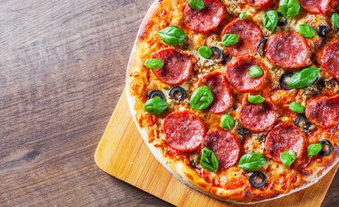 Pepperoni Pizza Mozzarella peyniri, salam, domates, zeytin, biber, baharat ve taze fesleğen. Ahşap masa arka plan üzerinde İtalyan pizza