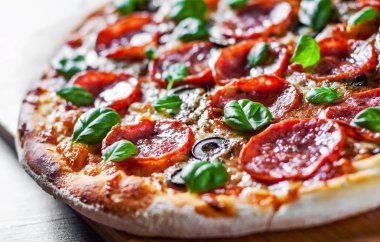 Pepperoni Pizza Mozzarella peyniri, salam, domates, zeytin, biber, baharat ve taze fesleğen. Ahşap masa arka plan üzerinde İtalyan pizza