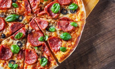 Pepperoni Pizza Mozzarella peyniri, salam, domates, zeytin, biber, baharat ve taze fesleğen. Ahşap masa arka plan üzerinde İtalyan pizza