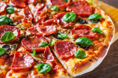 Pepperoni Pizza Mozzarella peyniri, salam, domates, zeytin, biber, baharat ve taze fesleğen. Ahşap masa arka plan üzerinde İtalyan pizza